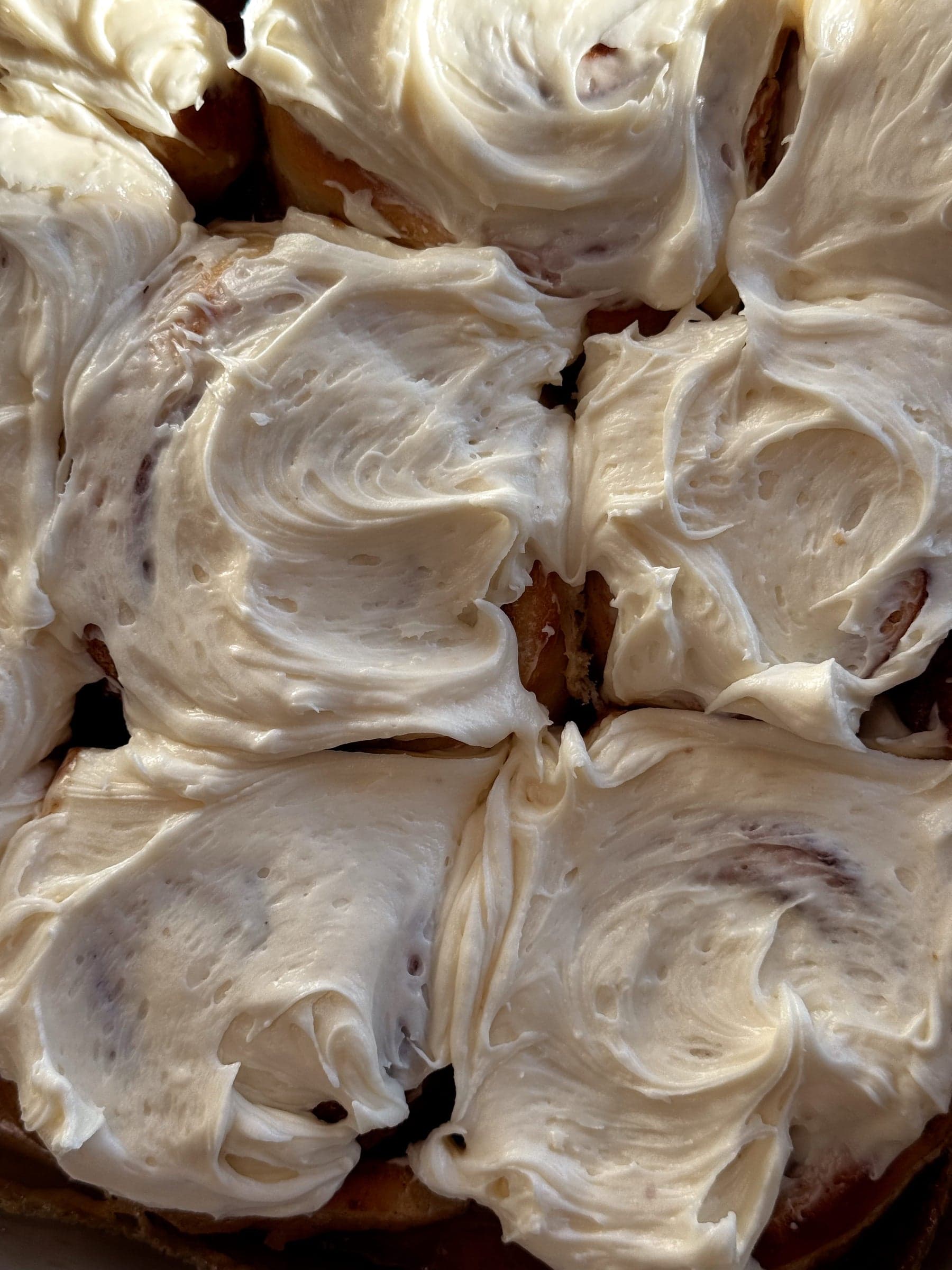 A pan of Dough Lady cinnamon rolls buried in swoops of cream cheese frosting